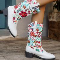 White boots with colorful floral patterns worn by a person on a wooden floor.