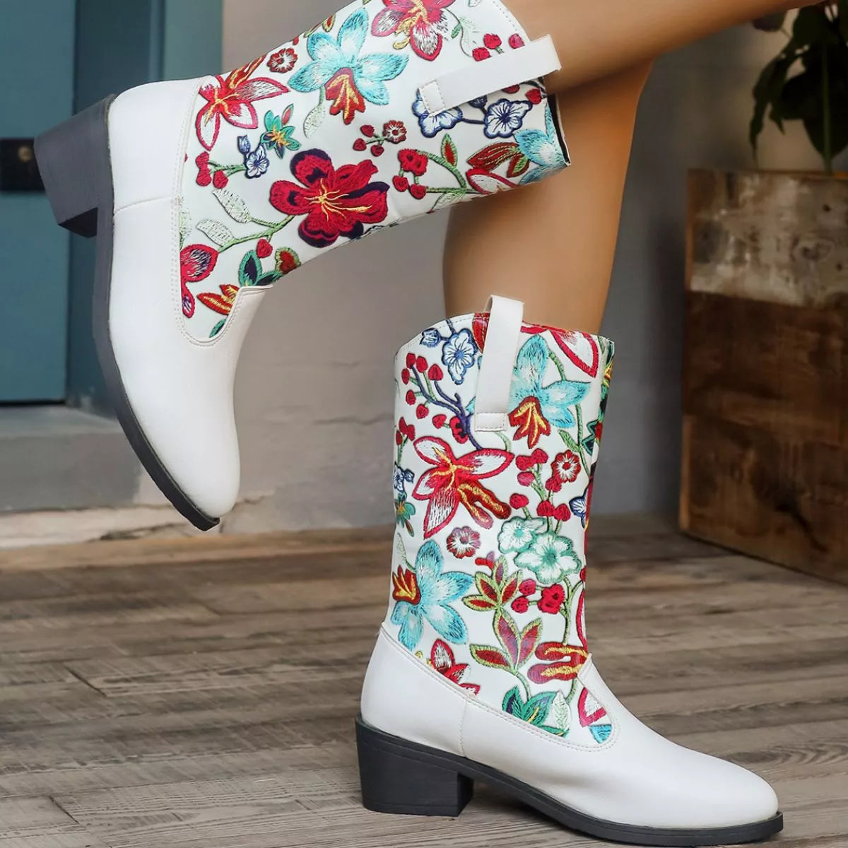 White boots with colorful floral patterns worn by a person on a wooden floor.