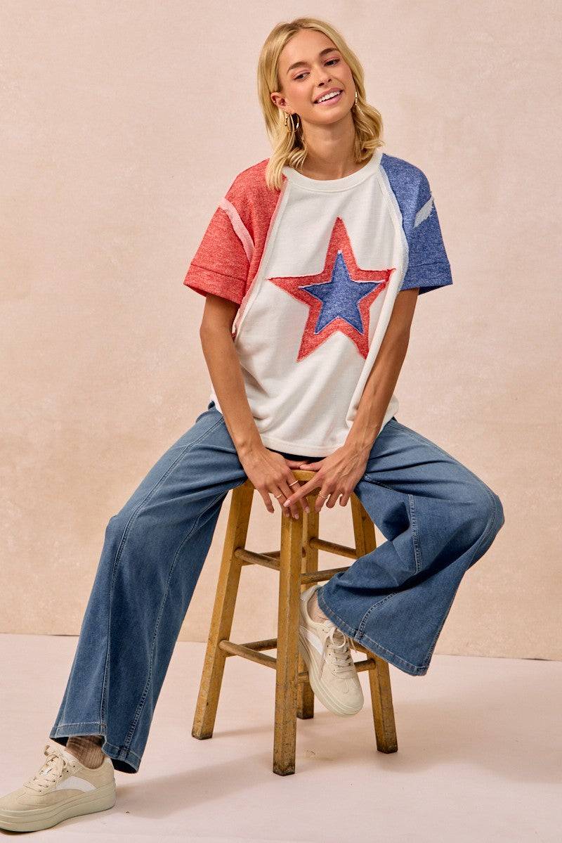 Woman sitting on a stool wearing a colorful t-shirt with a star design and jeans.