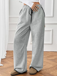 Person wearing gray sweatpants with a white wall background