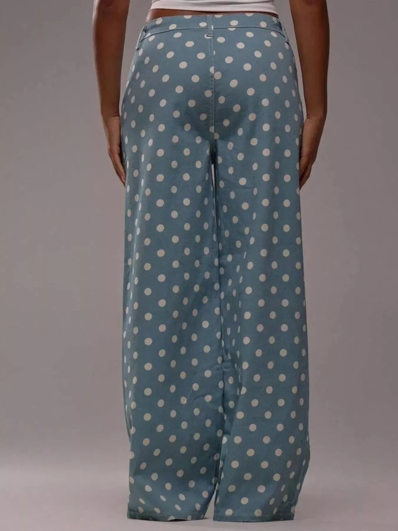 Blue pants with white polka dots worn by a person on a gray background