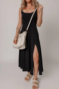 Woman wearing a black dress with a high slit, holding a white handbag against a plain background