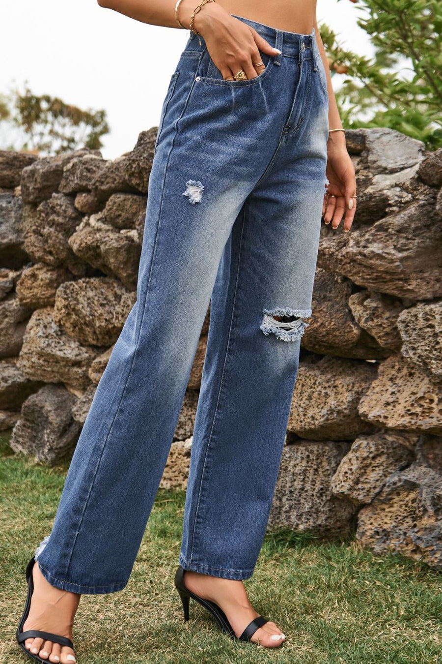 Person wearing blue jeans with a stone wall and grass background