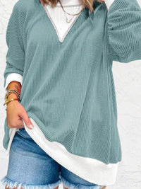 Person wearing a teal sweater over a white shirt with denim shorts on a white background