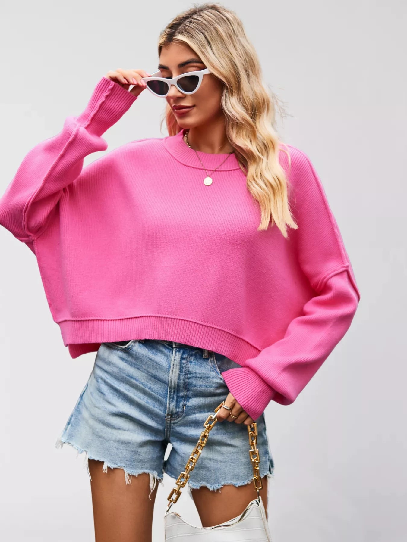 Woman wearing a pink sweatshirt and denim shorts against a plain background
