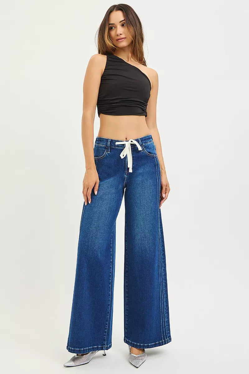 Woman wearing blue wide-leg jeans with a black top on a white background
