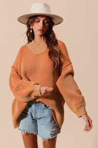 Woman wearing an orange sweater and denim shorts with a beige background
