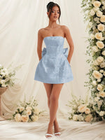 Woman in a light blue strapless dress standing in front of floral decorations.