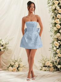 Woman in a light blue strapless dress standing in front of floral decorations.