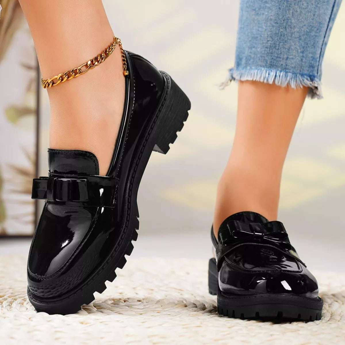 Black patent leather shoes with a bow detail worn by a person on a blurred background