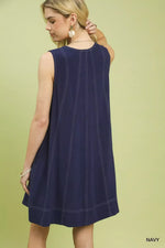 Woman wearing a navy sleeveless dress against a light green background