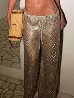 Person wearing sparkly gold pants holding a straw bag indoors.