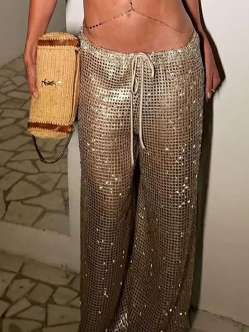 Person wearing sparkly gold pants holding a straw bag indoors.