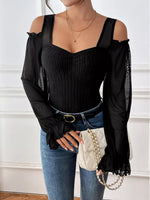 Woman wearing a black off-shoulder top with sheer sleeves and blue jeans, holding a white handbag.