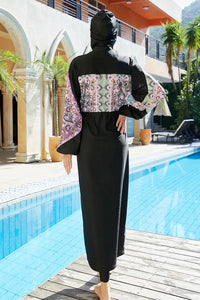 Person wearing a black abaya with a patterned design by a poolside.
