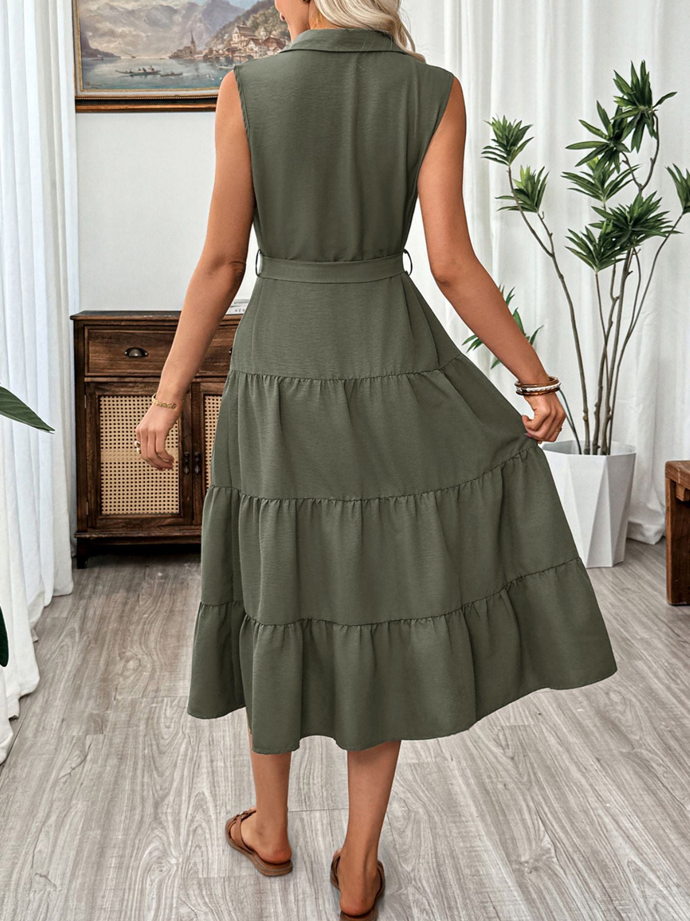 Woman wearing a green dress in a room with plants and furniture.