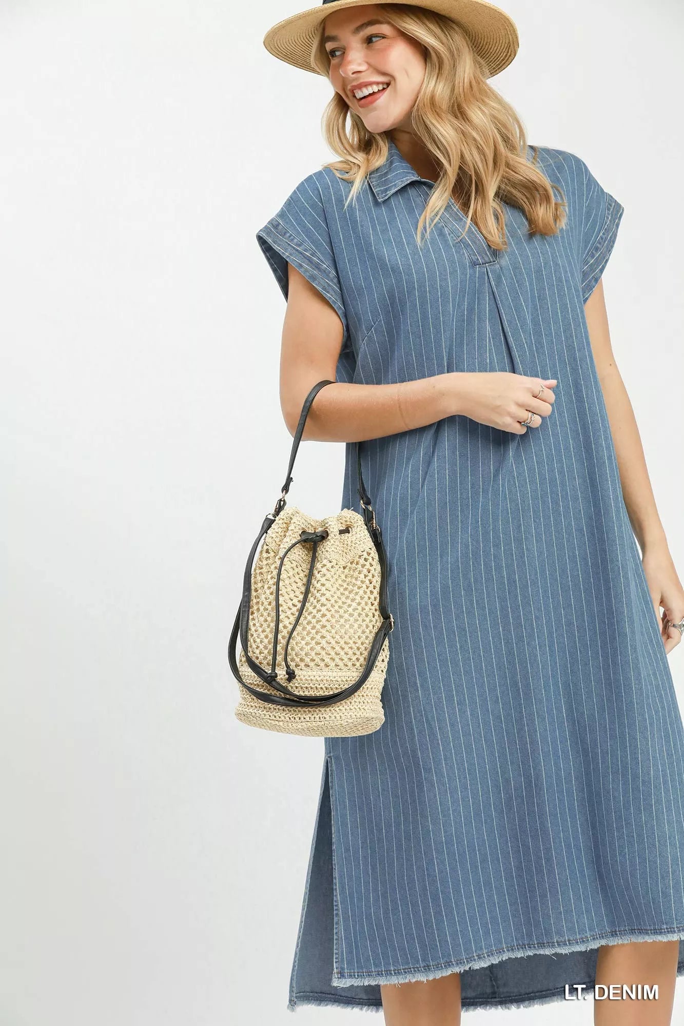 Woman wearing a blue striped dress holding a straw bag on a white background