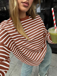 Person wearing a brown and white striped sweater holding a drink with a straw.