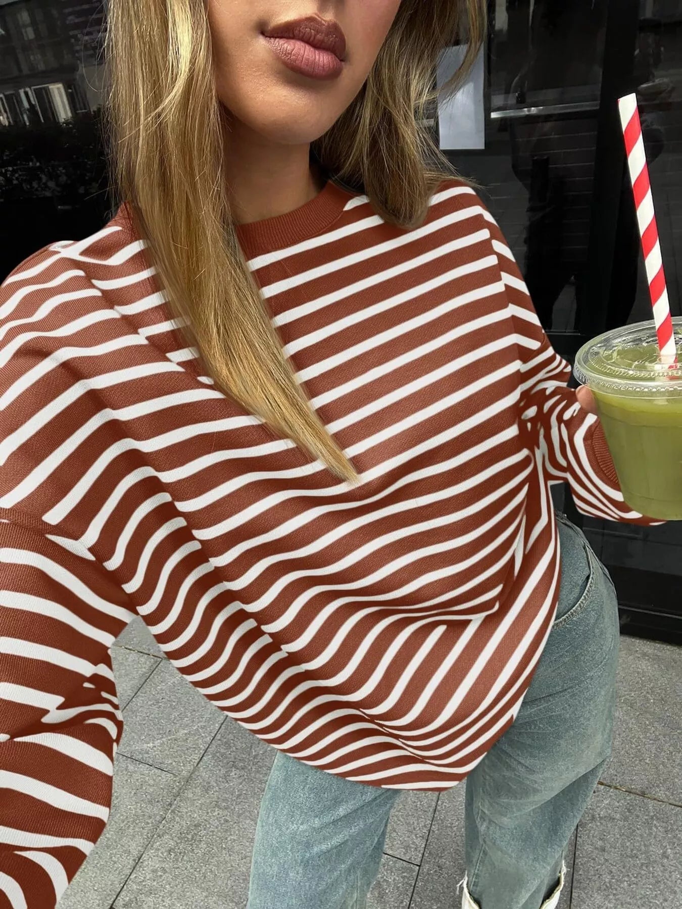 Person wearing a brown and white striped sweater holding a drink with a straw.