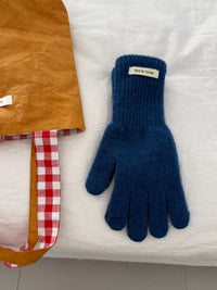 Blue knitted glove on a white surface with a brown fabric and red checkered strap in the background.