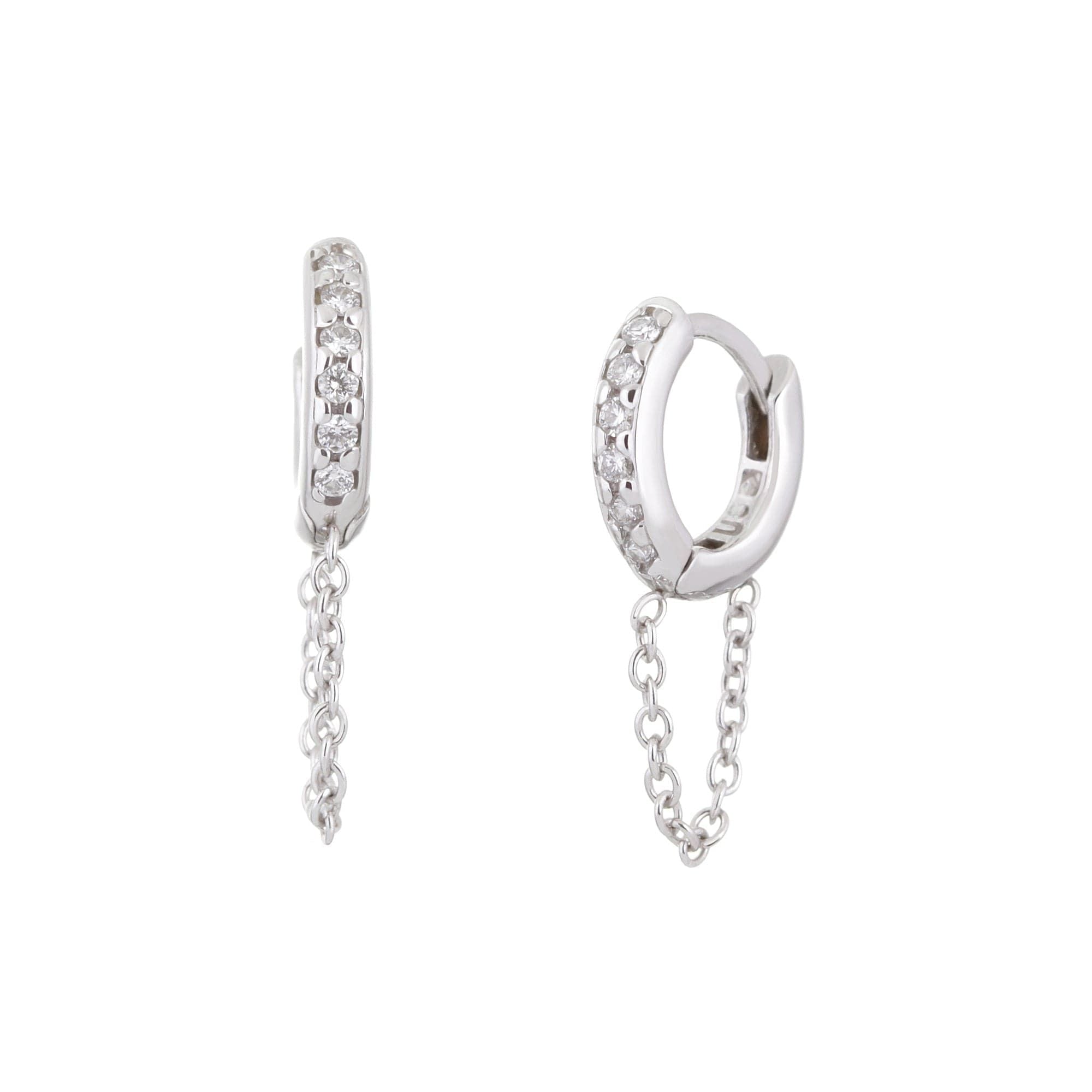 A pair of 14K white gold huggie hoops earrings with diamond accents and a white gold chain drop.