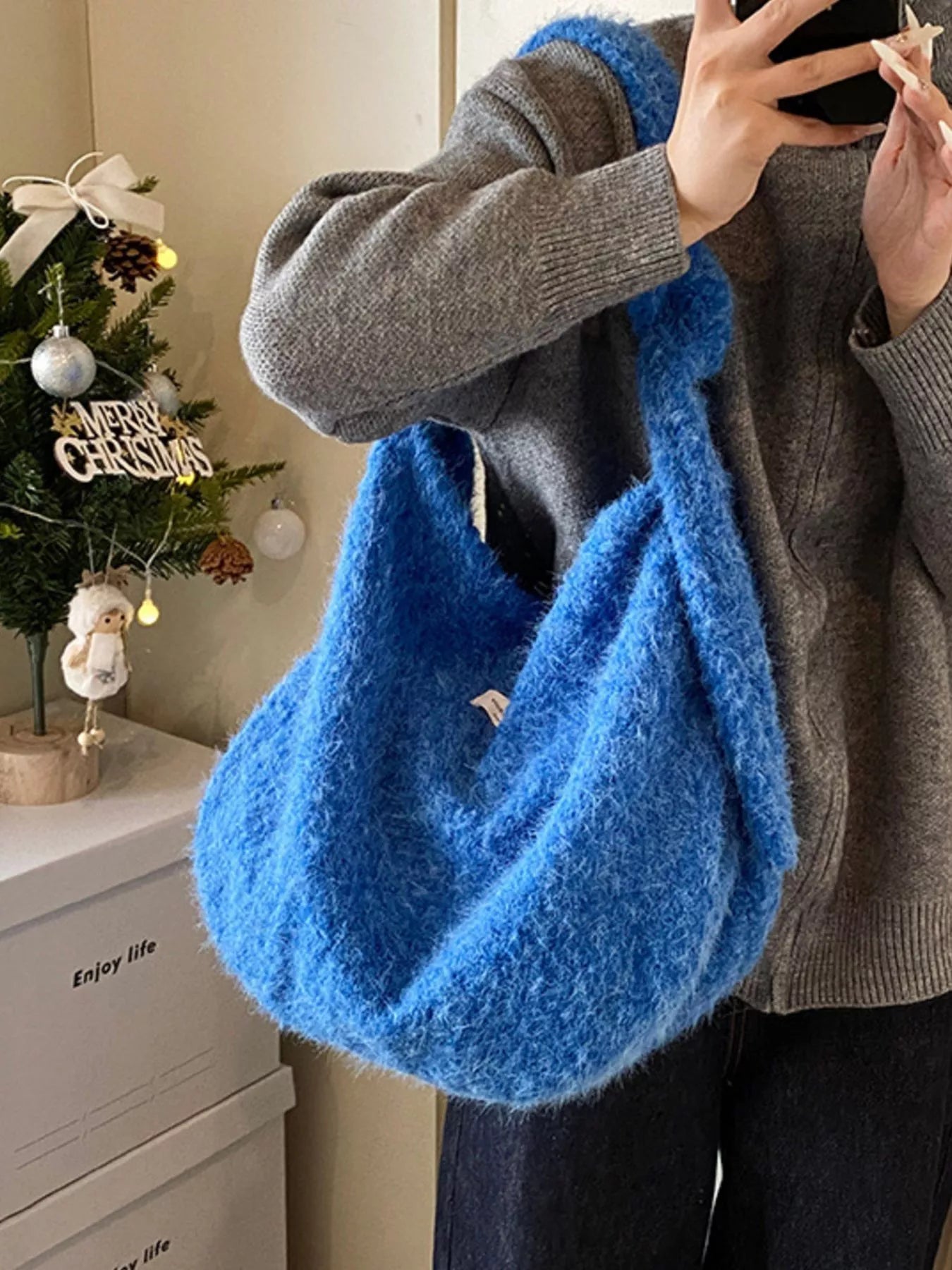 Person holding a blue fluffy bag with a Christmas tree in the background