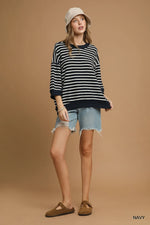 Woman wearing a striped sweater, denim shorts, and a hat on a beige background