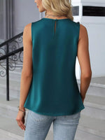 Woman wearing a teal sleeveless top and light blue jeans outdoors.
