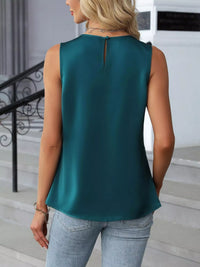 Woman wearing a teal sleeveless top and light blue jeans outdoors.