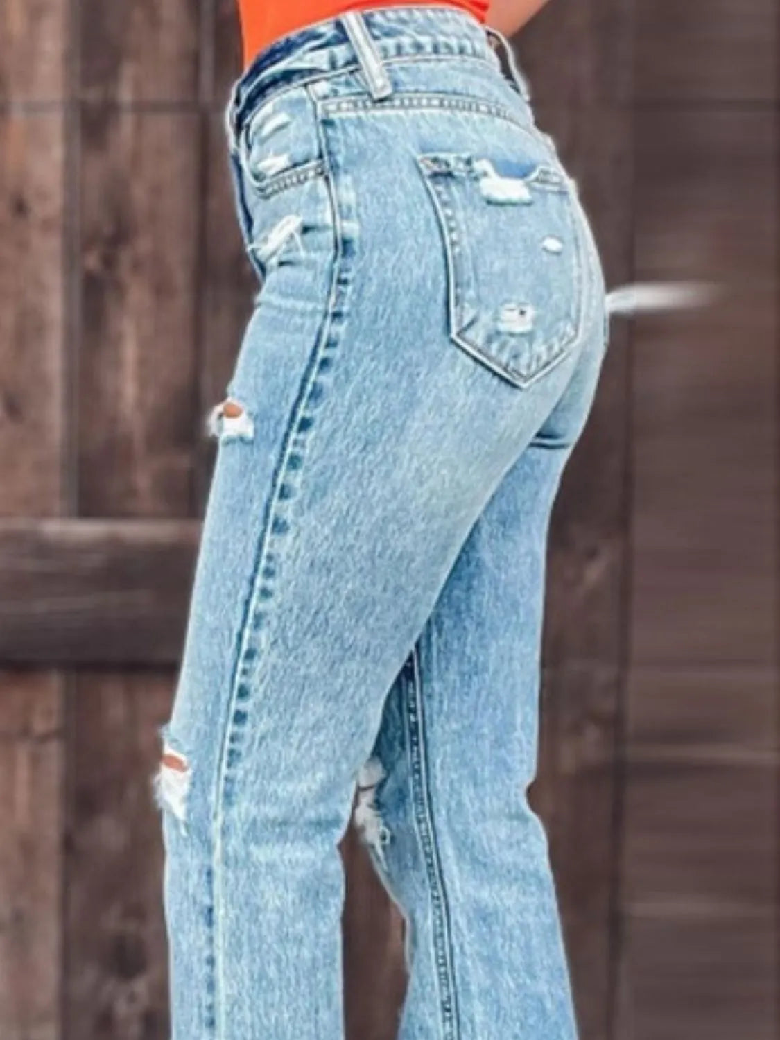 Ripped blue jeans worn by a person against a wooden fence background