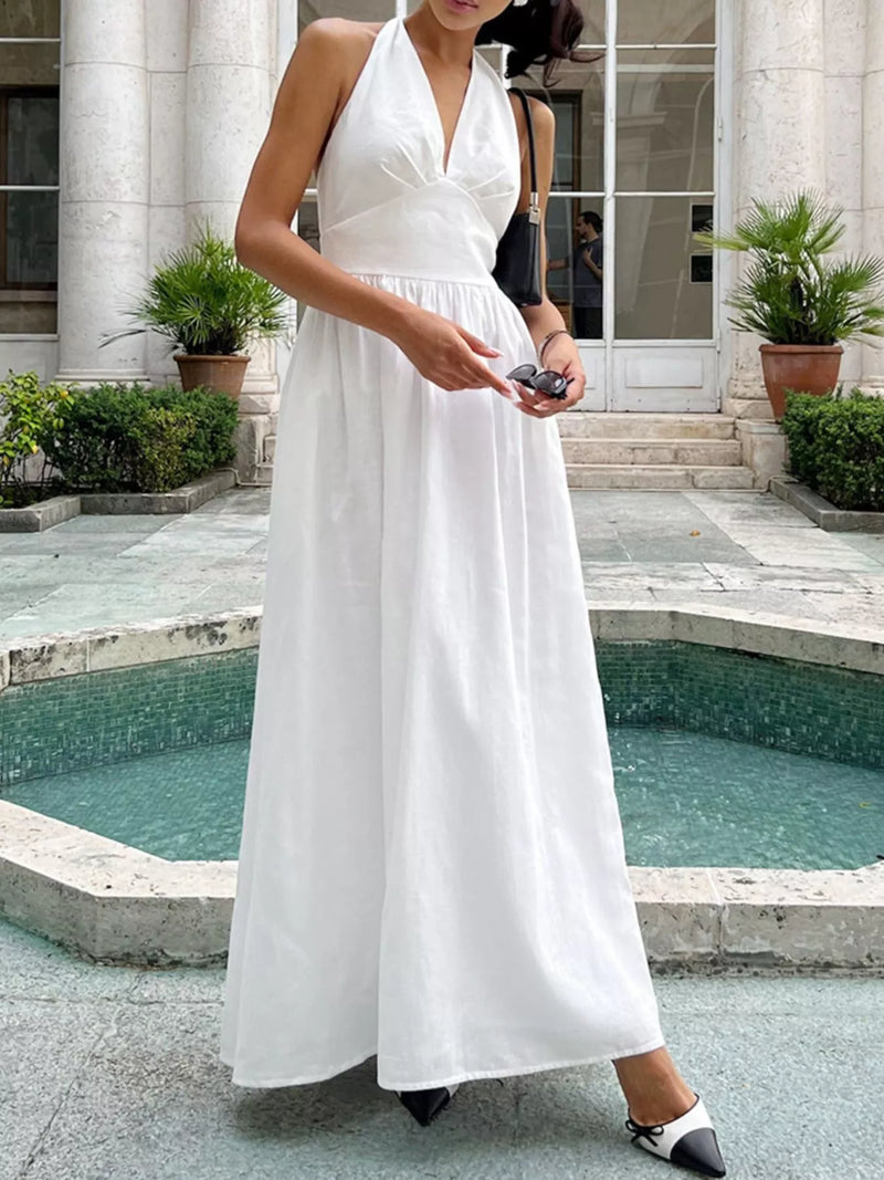 Woman in a white dress standing by a pool with classical architecture in the background
