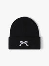 Black beanie with a white bow design on a light gray background