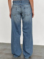 A person viewed from the back wearing light blue wide-leg denim jeans, standing against a plain off-white wall and gray floor.