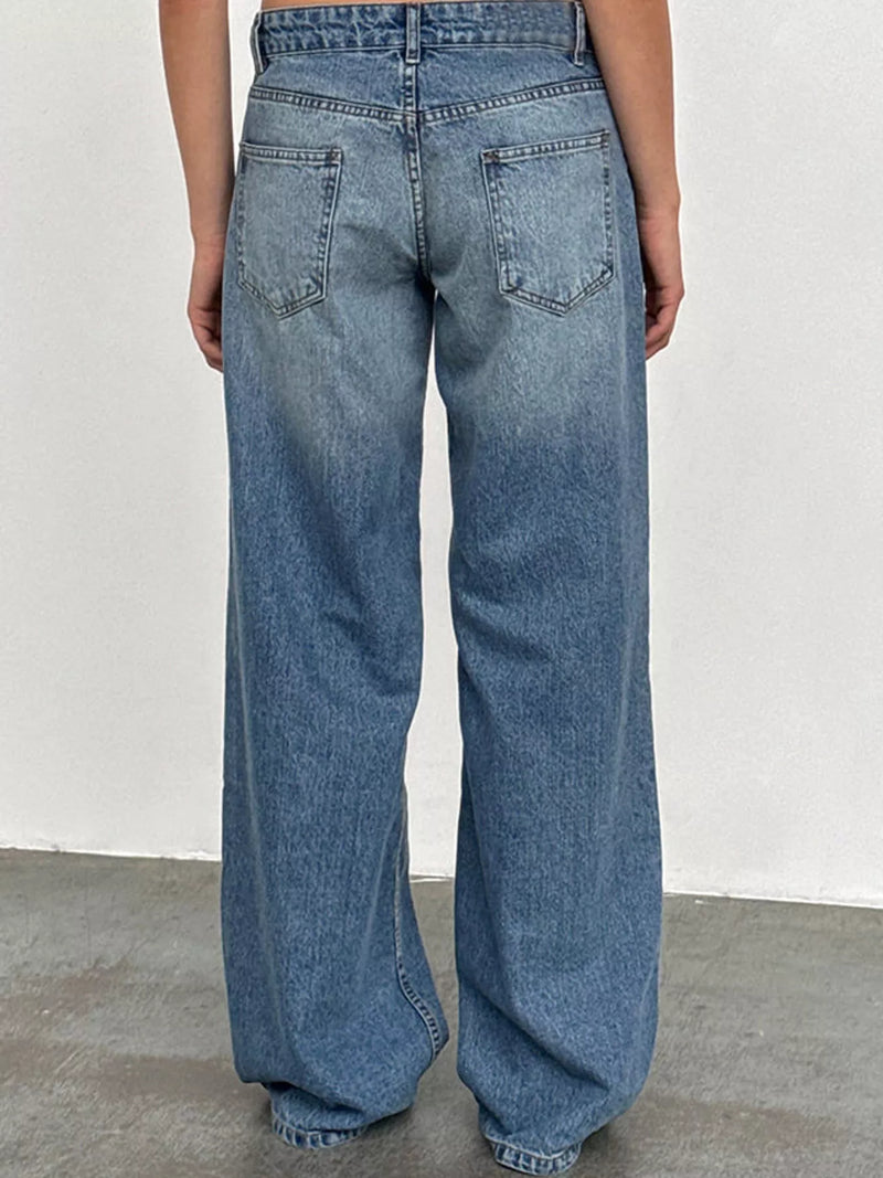A person viewed from the back wearing light blue wide-leg denim jeans, standing against a plain off-white wall and gray floor.