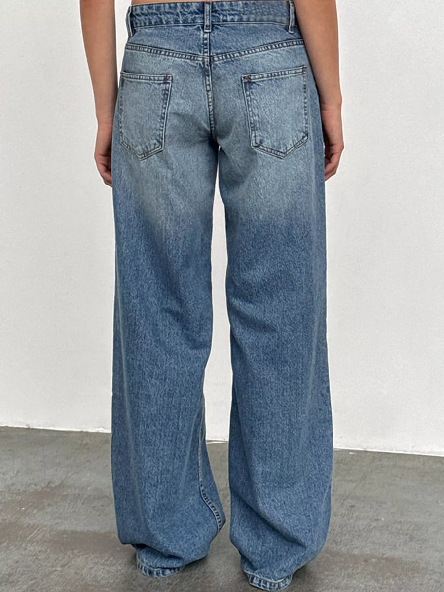 A person viewed from the back wearing light blue wide-leg denim jeans, standing against a plain off-white wall and gray floor.