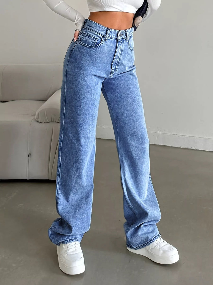 Person wearing blue jeans and white sneakers in a minimal indoor setting