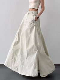 Person wearing a long light-colored skirt with a plain background