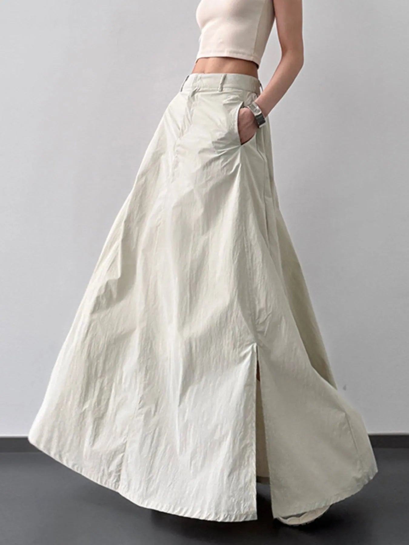 Person wearing a long light-colored skirt with a plain background