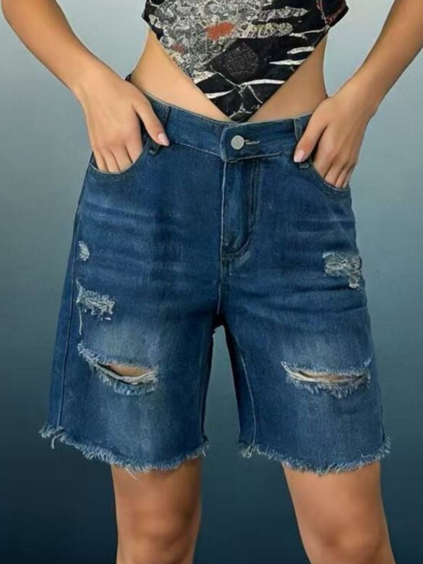 Person wearing distressed blue denim shorts on a gray background