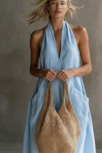 Woman in a light blue dress holding a woven bag against a neutral background