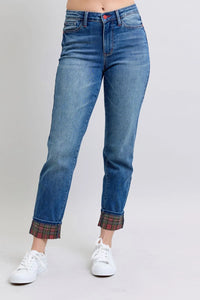 Blue jeans with plaid cuffs worn by a person on a light gray background