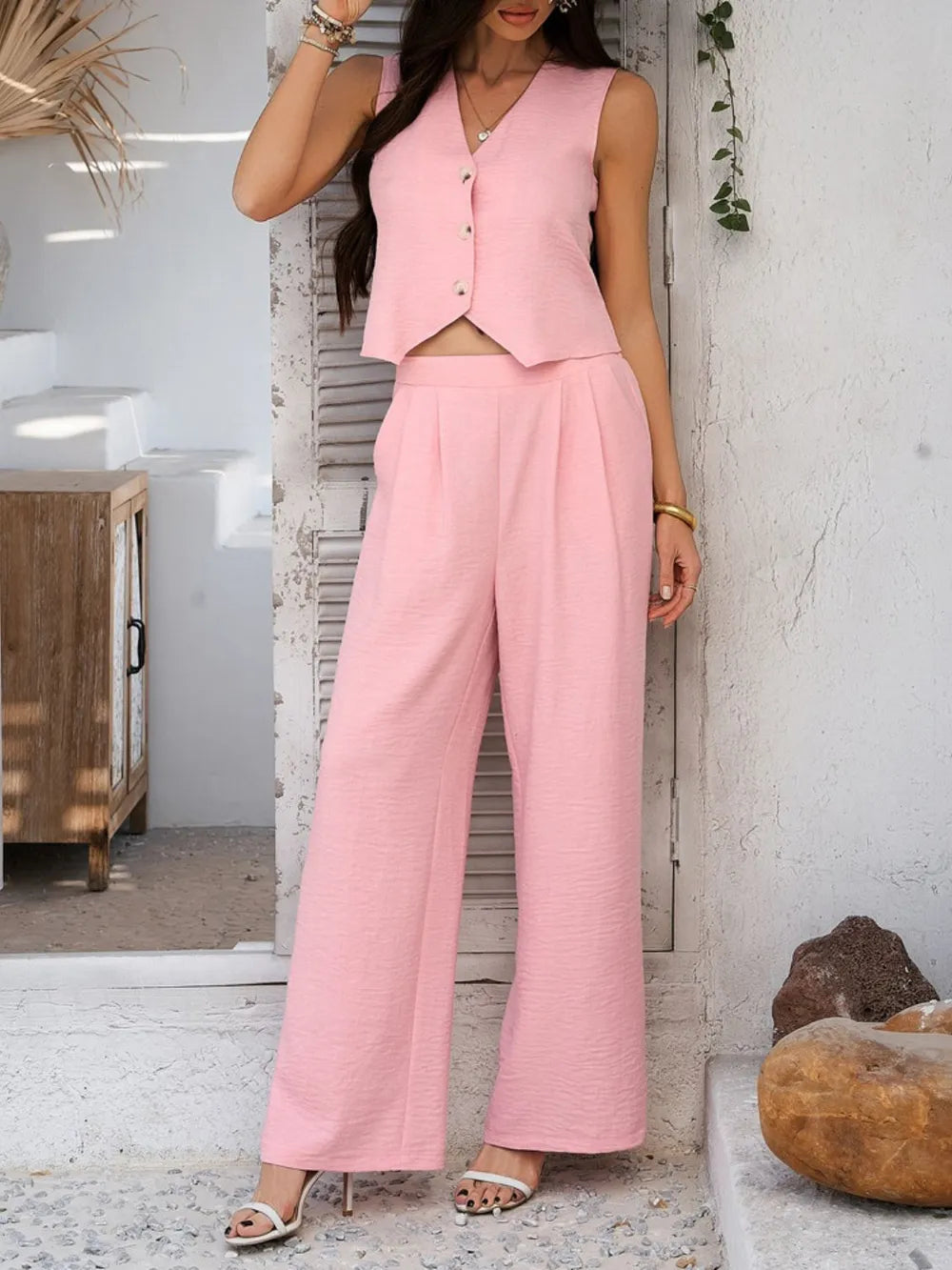 Woman wearing a pink outfit standing in a room with a white wall and wooden cabinet.