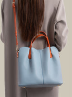 Light blue handbag with orange handles and strap held by a person wearing a gray outfit.