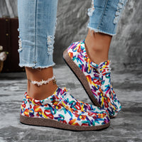 Colorful slip-on shoes with text pattern worn with ripped jeans on a gray surface.