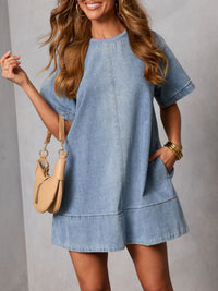 Woman wearing a denim dress holding a beige handbag against a gray background