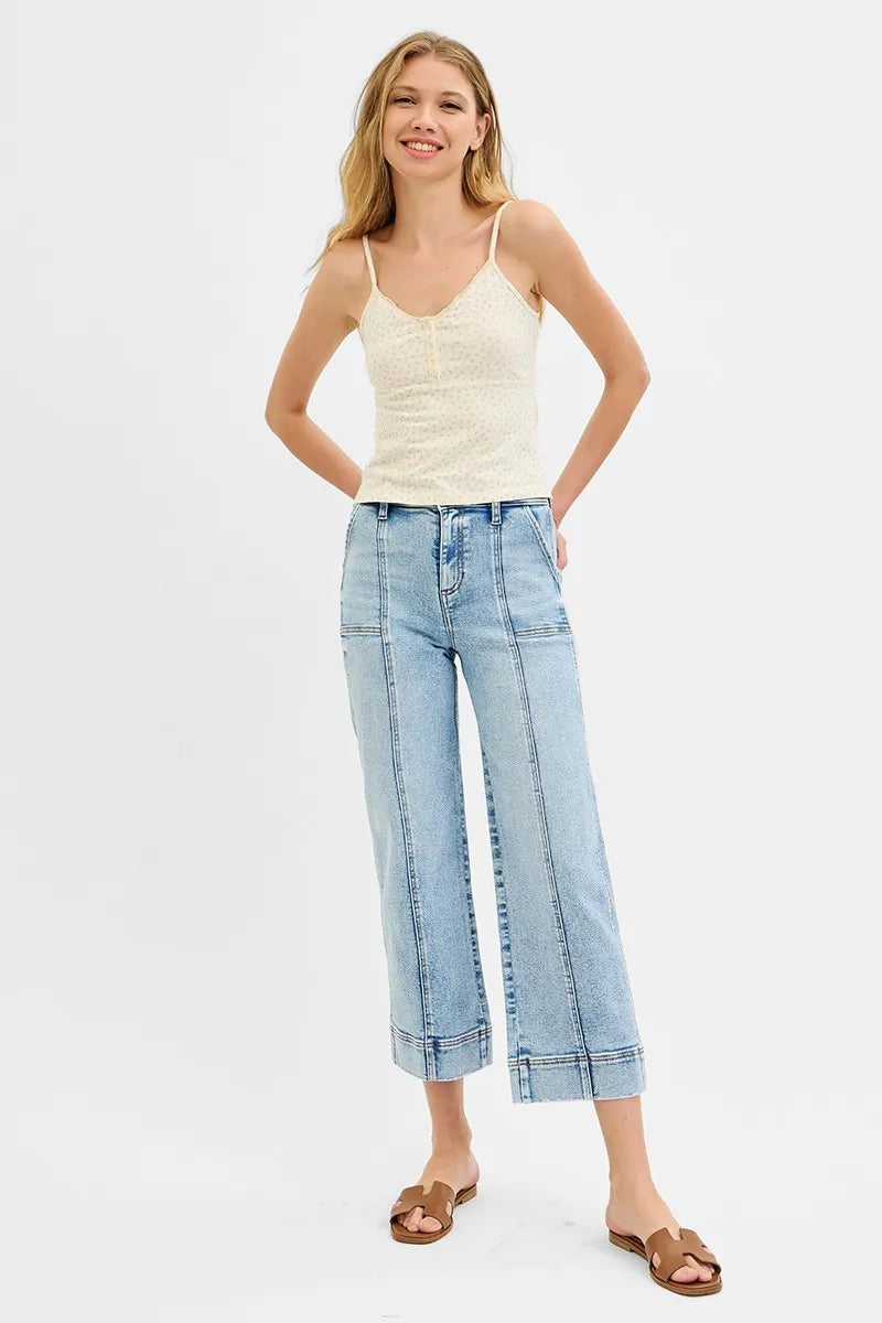 Woman wearing a cream tank top and light blue jeans on a white background