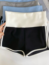 Black shorts with white trim held by a hand on a light gray background