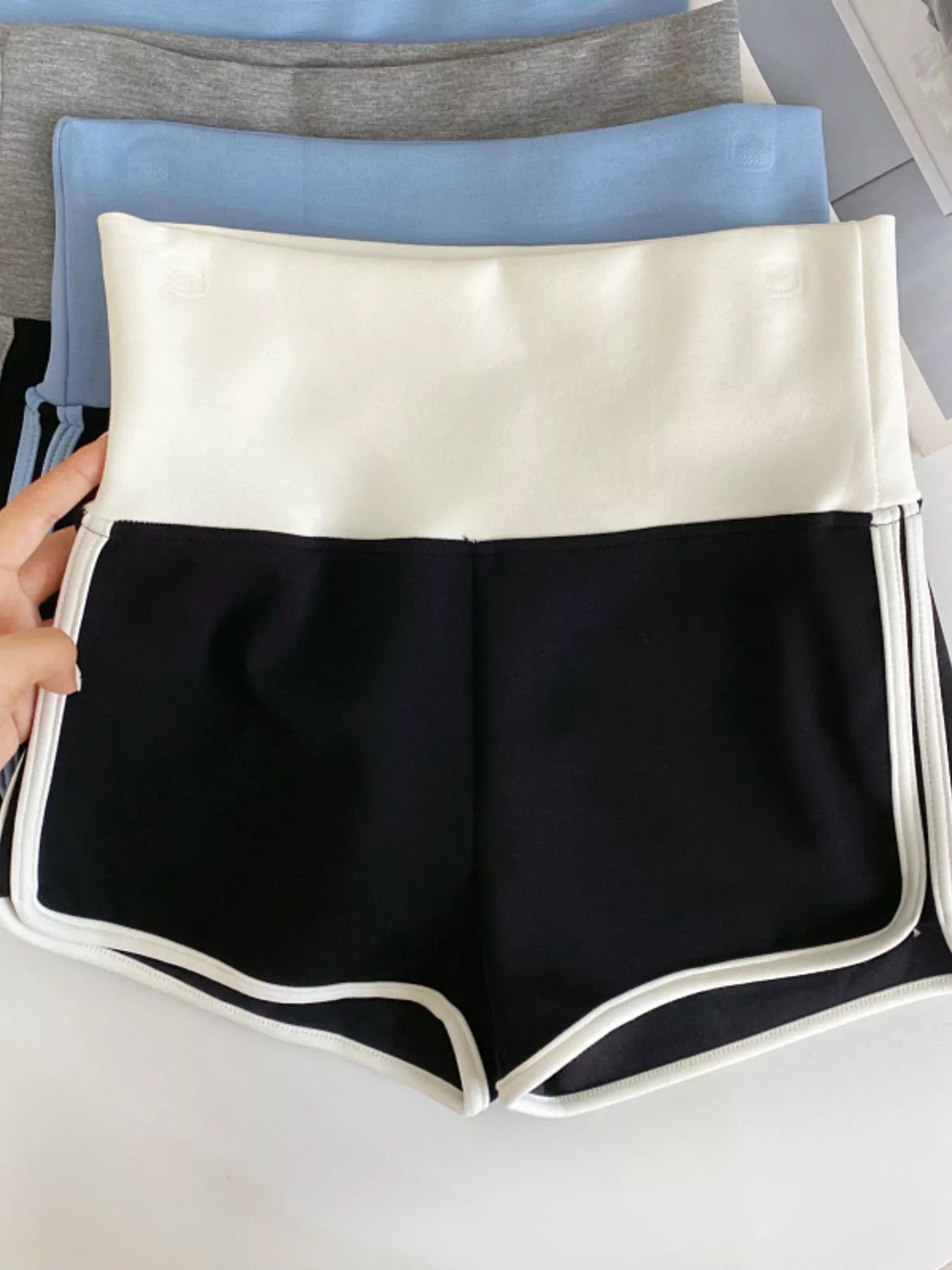 Black shorts with white trim held by a hand on a light gray background
