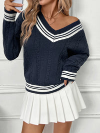 Woman wearing a navy blue sweater with white stripes and a white pleated skirt against a white wall.