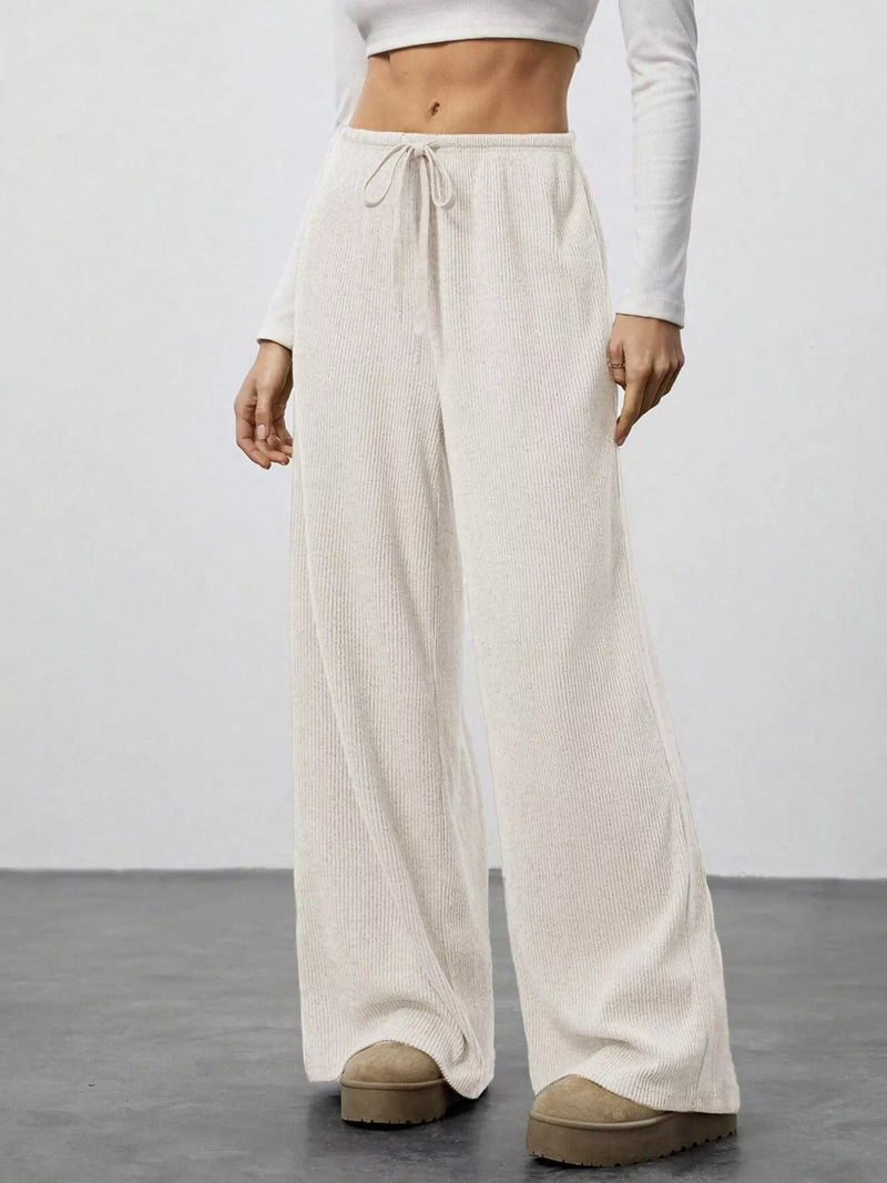 Person wearing beige wide-leg pants and white top on a plain background